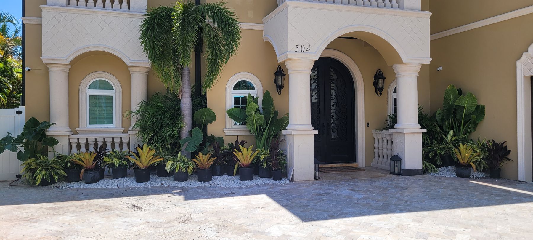 Luxury home grand entry with foxtail palm, elephant ears and bromeliad plantings over travertine pavers