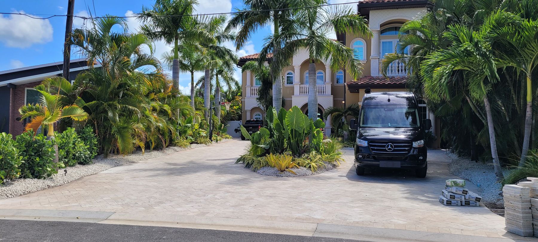 Royal palm lined travertine driveway at a Mediterranean estate home with layered tropical beds